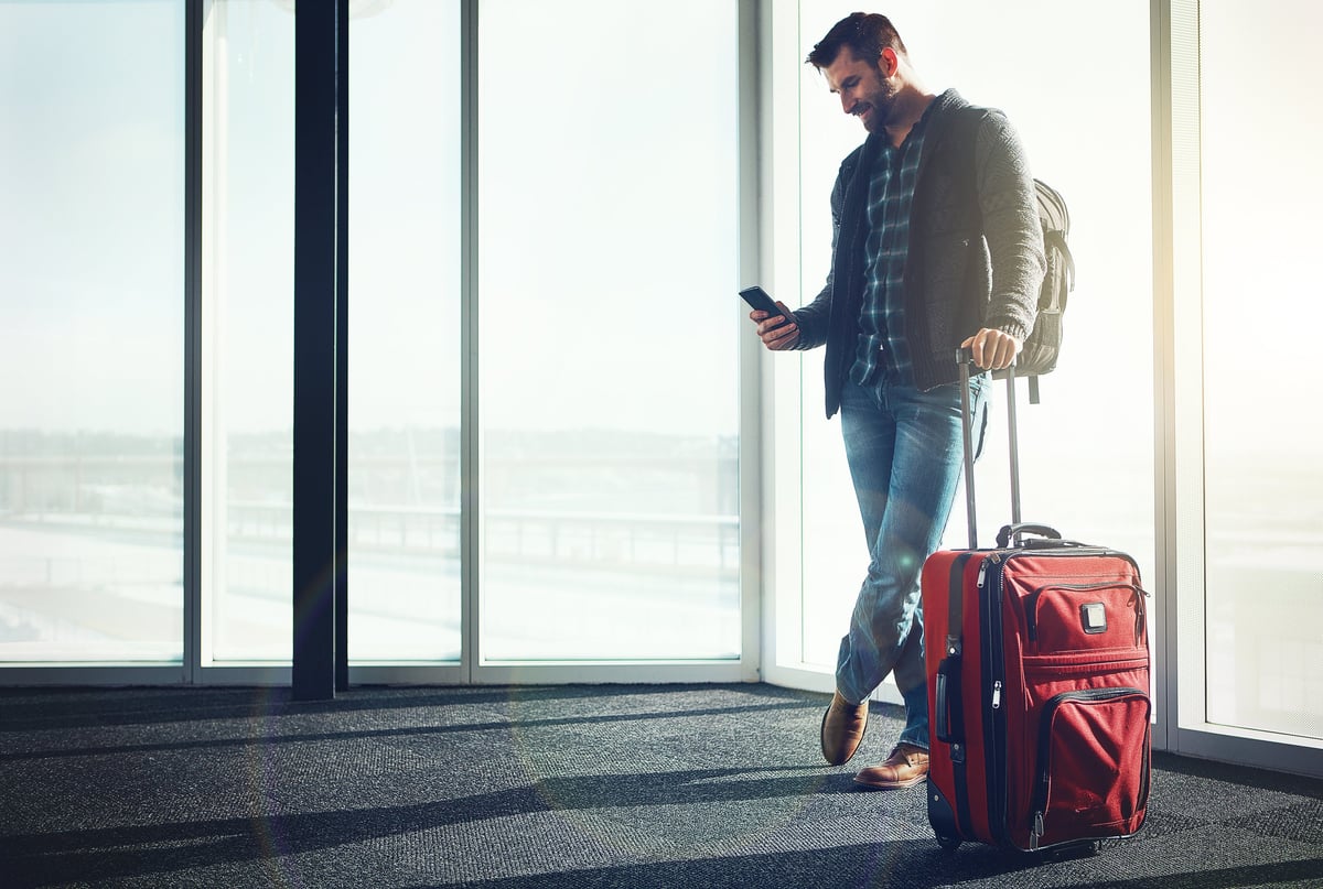 Traveler standing in an airport with luggage, looking at a smartphone